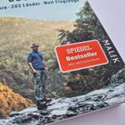 SPIEGEL Bestseller, Jetzt als Taschenbuch. 10 Jahre, 203 Länder, Null Flugzeuge. Ein Mann steht in einer waldigen Landschaft.