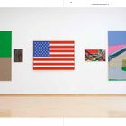 Texte: "1. Obergeschoss Raum 15".  
Abstrakte Gemälde an einer weißen Wand, darunter eine USA-Flagge.