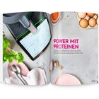 "POWER MIT PROTEINEN. Küchenmaschine und Zutaten wie Eier, Linsen, Kräuter und Besteck, auf einer offenen Doppelseite."