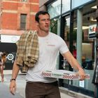 Auf einem weißen T-Shirt steht "CLAREMONT PIZZA". Ein Mann trägt eine Pizza-Schachtel und ein Hemd über der Schulter.