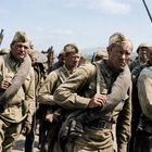 Soldaten in olivgrüner Uniform, tragen Gewehre und Vorräte auf den Schultern, marschieren in Formation.