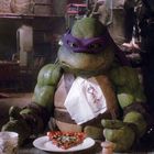 Serviette zeigt "Call Domino's Pizza". Eine humanoide Schildkröte mit lila Maske isst Pizza in einem dunklen Raum.