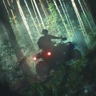 Ein verschwommener Fahrer auf einem Quad fährt durch einen nebligen Wald, beleuchtet von Sonnenstrahlen durch die Bäume.