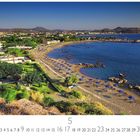 Text: "Faliraki Beach"
Klares Meer, sandiger Strand mit blauen Sonnenschirmen, grüne Vegetation, im Hintergrund Berge und Gebäude.