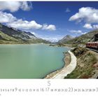 "Lago Bianco" und der Monat Mai sind abgebildet. Ein roter Zug fährt entlang eines türkisfarbenen Sees in einer Berglandschaft.