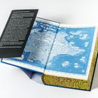 Text: Willkommen zur 125. Aufnahmprüfung... Karte einer Fantasiewelt in Blau, offene Buchseite, reich verzierter Einband.