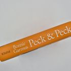 Buchstapel, oben ein Buch mit „Peck & Peck“ von Bonnie Garmus. Gelber Hintergrund, schwarzes Bildmotiv seitlich.