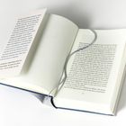Ein aufgeschlagenes Buch, links steckt ein Blatt mit Text. Ein graues Stoffband liegt lose über den Seiten.