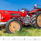 Text "Schlüter Super 350". Ein roter Traktor steht auf einer Wiese unter blauem Himmel. Unten ist ein Kalender für Mai.