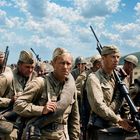 Eine Gruppe Soldaten in schmutziger Uniform, marschierend unter einem blauen Himmel mit vielen Wolken.