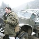 Auf einem verschneiten Gelände steht ein Lastwagen mit der Aufschrift "U.S.A. 275057". Daneben steht ein Mann in militärischer Kleidung, telefoniert und hält eine Karte.