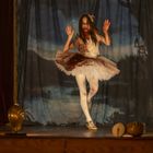 Ein Mädchen in einem Blut-befleckten Ballettröckchen tanzt vor einem theatralischen, düsteren Waldhintergrund.