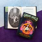 "Ghost Guild: The Lost Three" von Annie Barrows, illustriert von Chloe Bristol. Ein Buch liegt auf einem geöffneten anderen Buch.