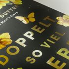 „Doppelt so viel Leben“ prangt groß auf einem dunklen Hintergrund, umgeben von gelben Blumen und einem Schmetterling.