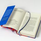 Ein aufgeschlagenes Buch mit Text auf Deutsch, ein blaues Lesezeichen und ein Booklet mit gelbem Text auf blauem Hintergrund.
