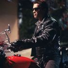 Eine Person in schwarzer Lederjacke und Sonnenbrille sitzt auf einem roten Motorrad in der Dunkelheit.