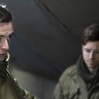 Drei Männer in Militärkleidung in einem Gespräch, ernste Mienen, einer trägt eine Uniform mit Abzeichen, ein anderer eine Mütze.