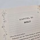 KAPITEL 51, NOLY. Bläschenmuster am Seitenrand, Text auf einer aufgeschlagenen Buchseite.