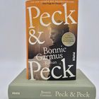 "Peck & Peck", Bonnie Garmus, Roman. Ein Buch steht auf einem anderen mit demselben Titel. Cover in Orange mit Porträt.