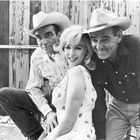Drei Personen, zwei Männer mit Cowboyhüten, eine Frau mit blonden Locken, alle lächeln. Hintergrund: Holzwand.