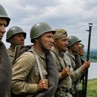 Eine Gruppe von Soldaten in Uniform und Helmen steht mit Gewehren, blickt konzentriert in die Ferne, im Hintergrund eine Flusslandschaft.
