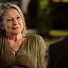 Eine ältere Frau lächelt sanft während eines Gesprächs im Freien, mit warmer Beleuchtung im Hintergrund.
