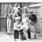 Auf dem Foto sind sieben Personen vor einer Holzwand. Ein Mann steht auf einer Leiter, eine Frau sitzt vorne in der Mitte.