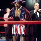 Ein Boxer trägt einen hohen Hut mit US-Flaggendesign und passenden Shorts. Er steht im Ring, umgeben von anderen Personen.