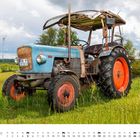 „September“ steht unten. Ein blauer Traktor mit roten Rädern steht auf einer Wiese, im Hintergrund ein Windrad.