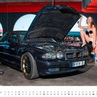„twinbusch.de“ steht links auf einer blauen Hebebühne. Eine Frau posiert neben einem geöffneten Auto.