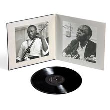 Eine Schallplatte vor einem geöffneten Albumcover mit Fotos eines Mannes, der eine Gitarre spielt.