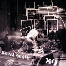 Texte: "Elliott Smith" und "XO". Mehrere überlagerte Fotos von Personen und einem Tonstudio.