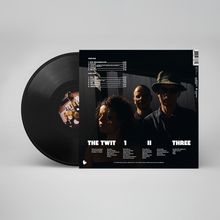 Schwarze Schallplatte mit Cover. Songliste auf Englisch und Deutsch. Drei Personen abgebildet, teils im Schatten.
