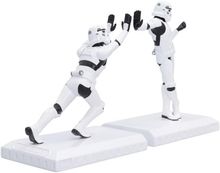 Zwei weiße, schwarz-akzentuierte Figuren mit Helmen machen einen High-Five auf weißen Sockeln. Science-Fiction-Thema.