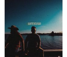 Der Text "WATERTOWN" schwebt über zwei Menschen am Ufer eines Sees, silhouettiert gegen den klaren Himmel.
