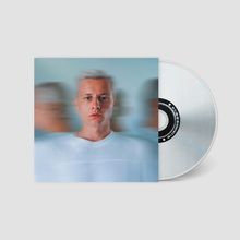 Ein Mann mit blondem Haar schaut direkt, unscharfe Mehrfachbilder links und rechts, grauer Hintergrund, daneben eine CD.