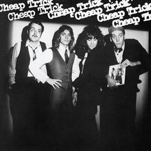 Text "Cheap Trick" mehrfach oben. Vier Männer in Anzügen, einer hält ein Foto. Schwarz-weiß.