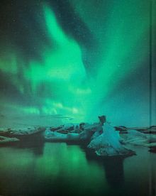 Keine erkennbaren Texte. Nordlichter über einer ruhigen, eisbedeckten Landschaft mit Reflexionen im Wasser.