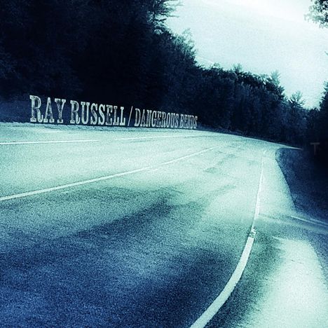 RAY RUSSELL / DANGEROUS BENDS. Eine leere Straße führt durch einen Wald.