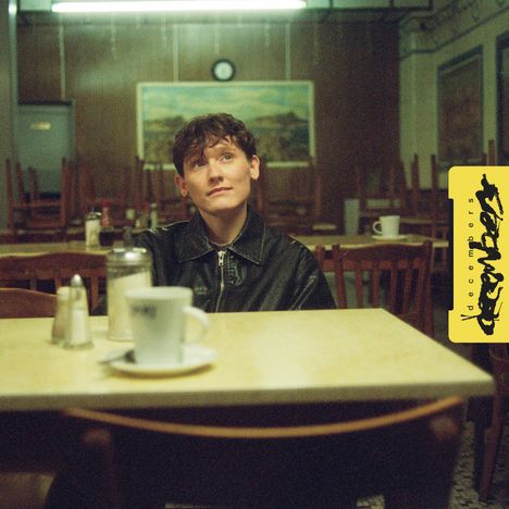 Text: „decembers“. Eine Person sitzt nachdenklich in einem leeren Café. Der Stil ist retro und gemütlich.
