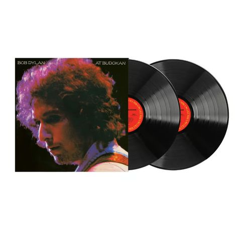 Text: "BOB DYLAN AT BUDOKAN". Zwei Schallplatten, ein Porträt eines Mannes mit lockigem Haar in farbigem Licht.