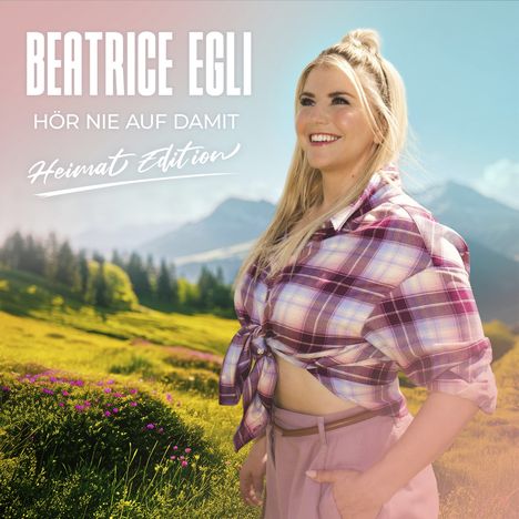 Beatrice Egli: Hör nie auf damit, Heimat Edition. Frau in kariertem Hemd auf Wiese, Berge im Hintergrund.