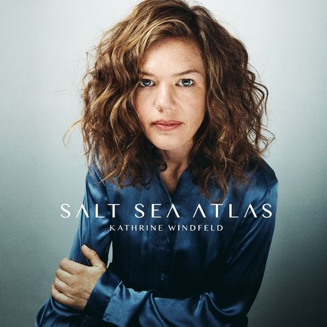 „Salt Sea Atlas“ und „Kathrine Windfeld“. Frau mit lockigen Haaren in blauer Bluse schaut direkt nach vorn.