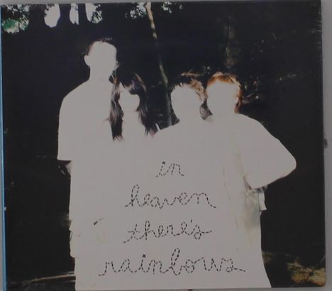 Der Text lautet: "in heaven there's rainbows". Vier Personen stehen nebeneinander, ihre Gesichter sind stark überbelichtet.