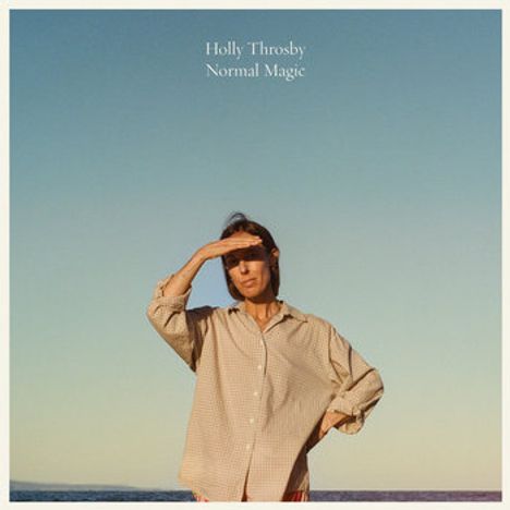 Text: "Holly Throsby Normal Magic". Eine Person steht am Meer, hält die Hand über die Augen und trägt ein lockeres Hemd.