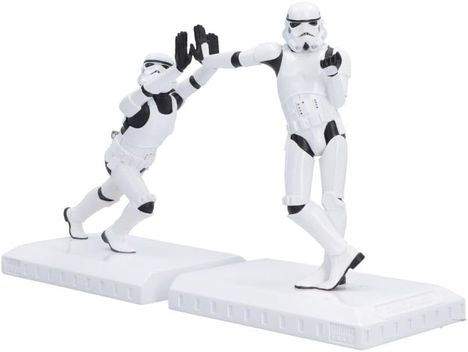 Zwei weiße Figuren in Rüstung, eine in Tanzpose, die andere im Sturz. Beide auf weißen Sockeln.