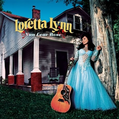 „Loretta Lynn, Van Lear Rose.“ Frau in blauem Kleid lehnt an Baum, Gitarre vor altem Haus mit Säulen.
