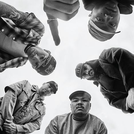 Es sind fünf Männer in einem Kreis, die in die Kamera blicken, teilweise mit Basecaps und Bandanas gekleidet.