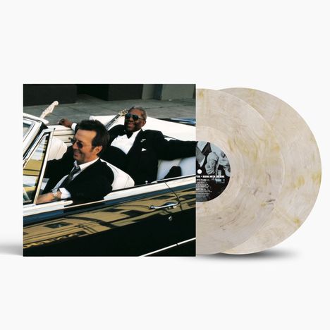 Zwei Männer in einem Cabrio, lächelnd. Ein Vinyl mit schwarzem Label ist teilweise sichtbar; keine weiteren Details zu erkennen.