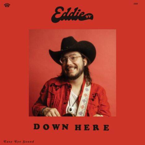 "Eddie 9V", "DOWN HERE". Ein Mann mit Cowboyhut und Brille, lächelt, trägt ein rotes Hemd, hält eine Gitarre vor rotem Hintergrund.